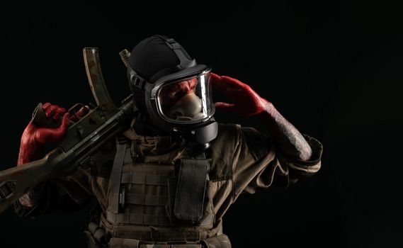 man in a military uniform and a gas mask holds a weapon with bloody hands with an angry expression of emotions