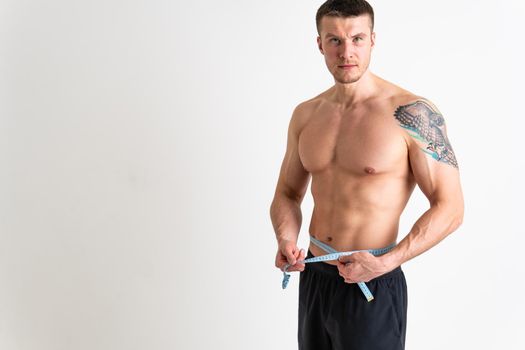 A man measures the waist of a metre and poses against a white background isolated body muscular hand, slim health abdomen slimming dieting, ifestyle person. Oss nutrition athlete, one sport attractive tape