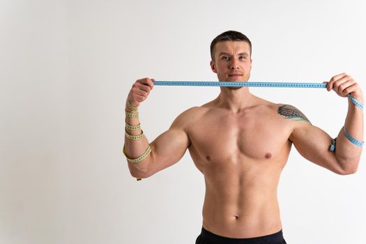 A man measures the waist of a metre and poses against a white background isolated young fitness healthy health meter ifestyle person. Measure care studio, one sport attractive tape