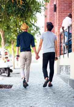 Shot of a young gay couple waling outdoors while holding hands.