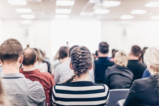 Business and entrepreneurship symposium. Speaker giving a talk at business meeting. Audience in conference hall. Rear view of unrecognized participant in audience.