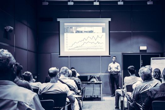 Speaker giving a talk in conference hall at business event. Unrecognizable people in audience at conference hall. Business and Entrepreneurship concept. Blue toned black and white.