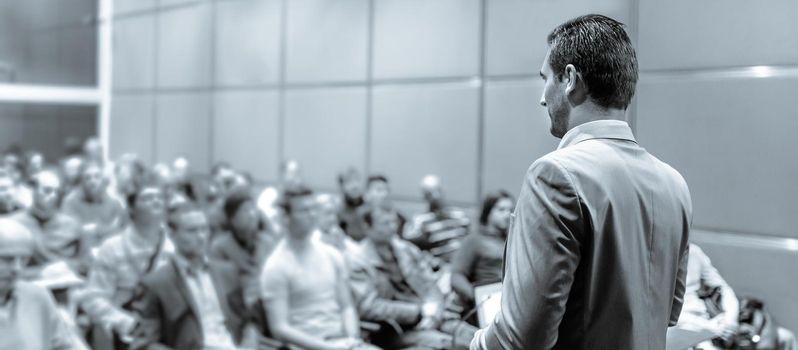 Speaker giving a talk on corporate business conference. Unrecognizable people in audience at conference hall. Business and Entrepreneurship event.