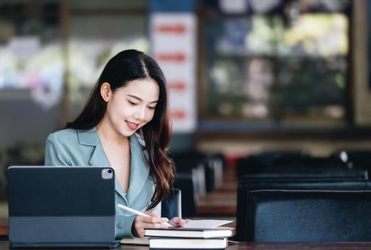 businesswoman showing a smiling face while reading a book developing financial and investing strategies and operating a computer tablet working on a wooden table