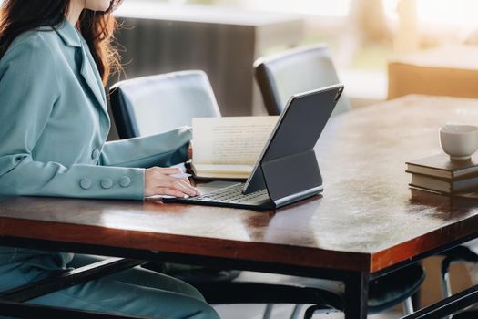 businesswoman showing a smiling face while reading a book developing financial and investing strategies and operating a computer tablet working on a wooden table