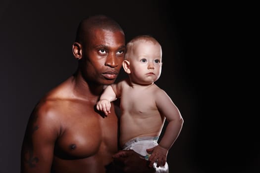Concept shot of a man holding a little boy in his arms against a black background.