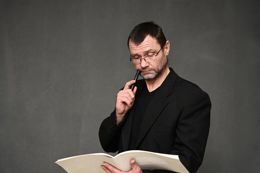 A businessman in a jacket looks into a folder in his hands. Portrait on a gray background in the studio