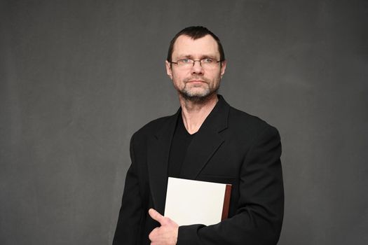 A businessman in a jacket looks at the camera with a folder in his hands. Portrait on a gray background in the studio