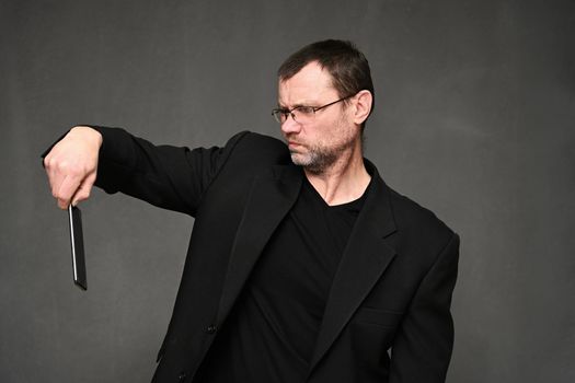 An adult businessman in a jacket looks at the smartphone with displeasure. Portrait on a gray background in the studio