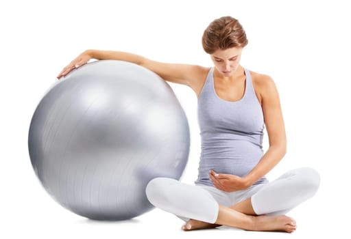A fit pregnant woman gazing down at her stomach while holding an exercise ball.