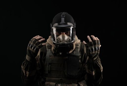 man in a military uniform and a gas mask holds with an angry expression of emotions on a black background