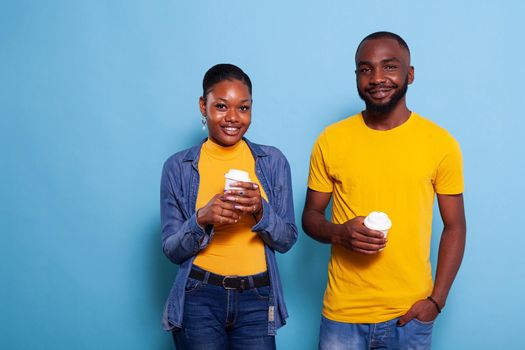 People in relationship smiling and holding cup of coffee in hand. Young couple enjoying hot beverage, expressing love feelings and looking at camera. Girlfriend and boyfriend in studio.