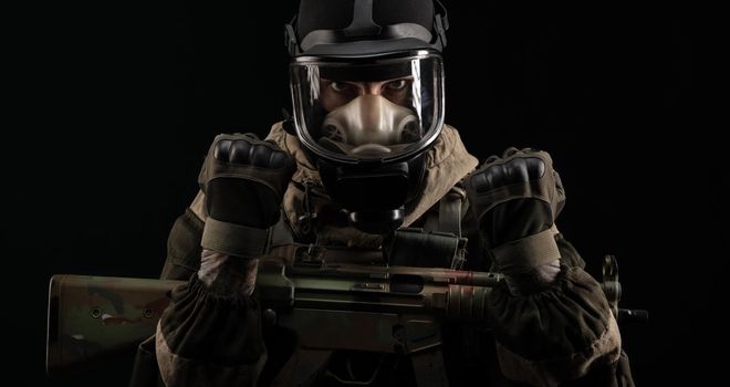 man in a military uniform and a gas mask holds a weapon with an angry expression of emotion