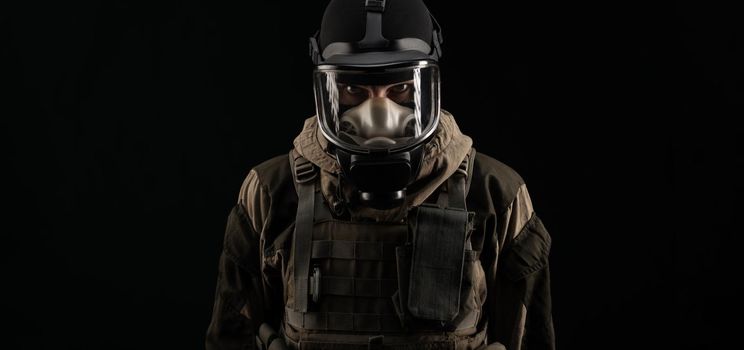 man in a military uniform and a gas mask holds with an angry expression of emotions on a black background