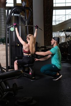 RUSSIA, MOSCOW - FEB 11, 2022: A girl is engaged in a led press simulator in a red blonde beautiful on a black background leg gym training man legs, for lifting strength from fit and sport bodybuilder, power length. Girl female sportswear, exercises trainer