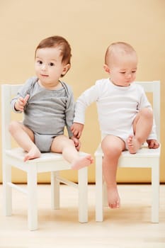 Adorable portrait of two cute babies sitting on chairs and smiling at the camera.