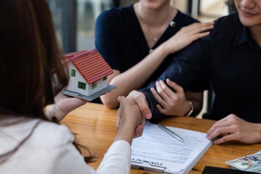 A happy young couple receives a wonderful bargain after signing a contract to purchase a home. Broker and customer shake hand after have a good deal. Real Estate concept