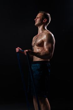 Man on black background keeps dumbbells pumped up in fitness bodybuilding sexy athlete muscular bodybuilder powerful, person weightlifting. Lift handsome adult, one fit With a ribbon in hand, the fitness gum is black