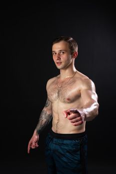 Man on black background keeps dumbbells pumped up in fitness bodybuilding biceps body muscular fitness bodybuilder powerful, shirtless weightlifting. handsome guy fit strains the presbytery muscles fingers point at us