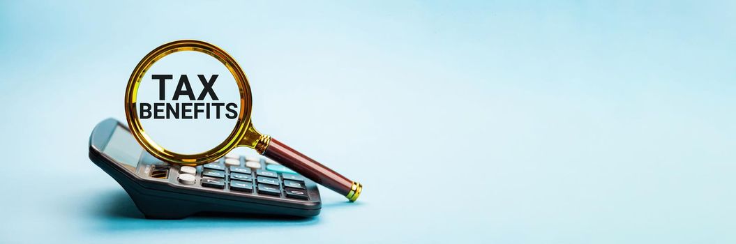TAX BENEFITS. The concept of finance and business. On the blue background lies a calculator and a magnifying glass with the inscription - TAX, counting bills or taxes, online banking services