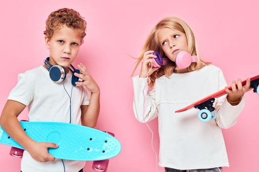 Funny children in headphones skateboards in hands pink color background. High quality photo