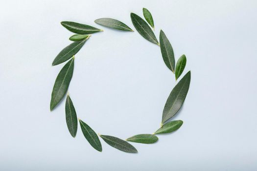 A circular wreath formed with olive leaves, forming a beautiful decorative and harmonious element, on a soft blue background