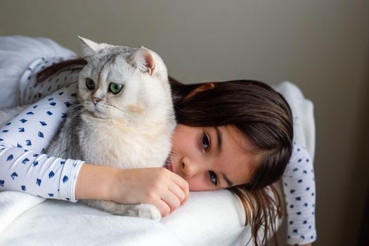 A little girl lies sad with a white cat on the edge of the bed, hugs him. Copy space