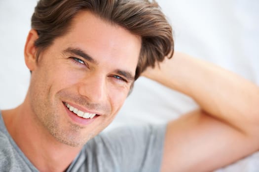 Portrait of a handsome young man lying in bed and leaning on his hands.