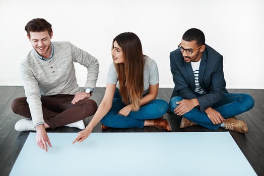 Studio shot of a group of young people sitting on the floor and working on blank paper.