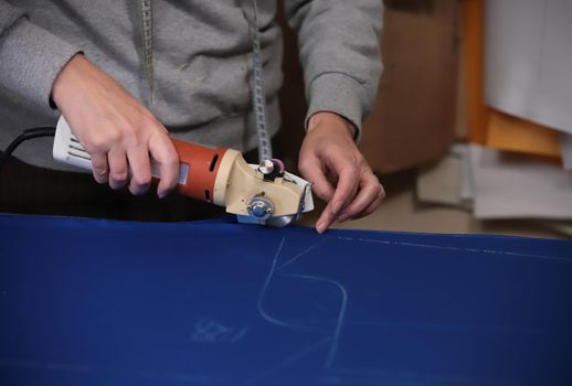 Worker cutting the cloth by sketching using the instrument. Only hands. Clothing industry