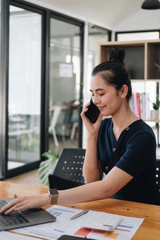 Portrait of asian businesswoman making phone call while working with laptop computer for accounting financeial