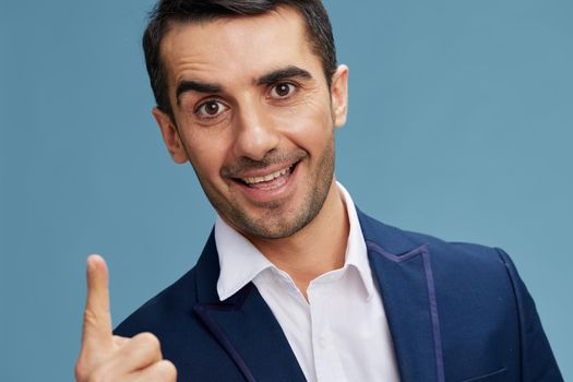 close-up portrait of a cheerful man in a blue business suit shows his index finger up blue background copy-space. High quality photo