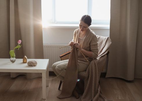 Young woman knitting in a cozy room at home.