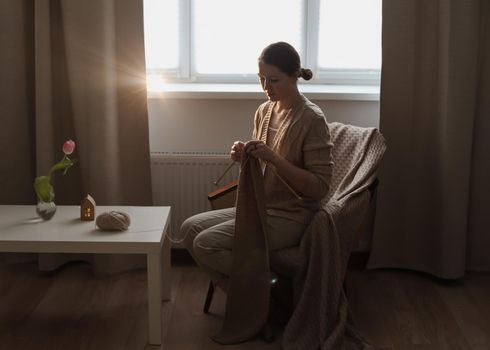 Young woman knitting in a cozy room at home.