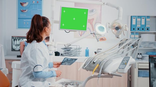 Dentist receiving teeth scan from man while looking at green screen on monitor. Specialist doing oral care examintion with radiography and isolated chroma key in dentistry cabinet