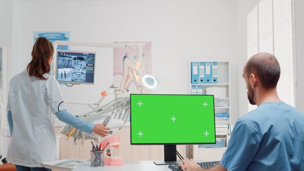Dental assistant using monitor with horizontal green screen in dentist office. Oral care specialists working with teethcare equipment and chroma key for isolated background in cabinet.