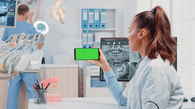 Woman working with horizontal green screen on mobile phone for teethcare in dentist office. Orthodontist looking at chroma key and mockup template on smartphone for dental care.