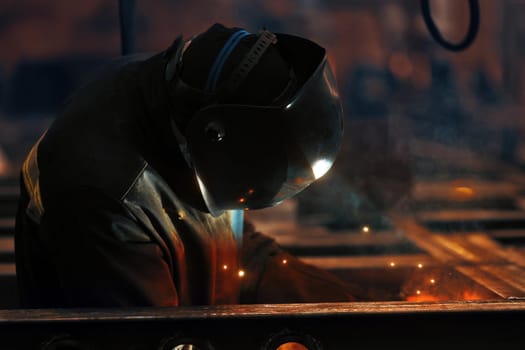 Welder at work. Welding of metal sparks and smoke in the workshop. Industrial Welder With gas Torch in Protective Helmet, welding metal profiles. The welding operation at construction site.