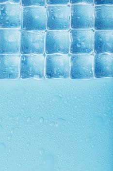 Ice made of cubes lined up with drops on a blue background with free space
