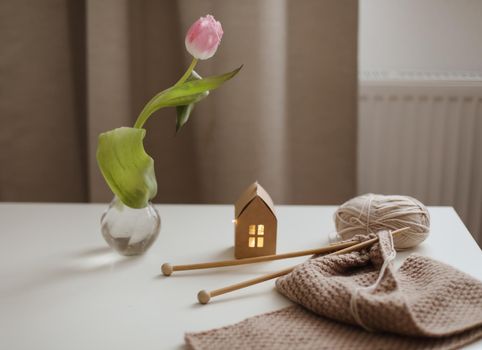 cozy home interior decor with a chair, plaid, table and knitting needles with threads, beige yarn.