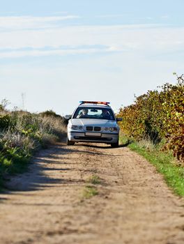 Shot of a police car driving down a dirt road.