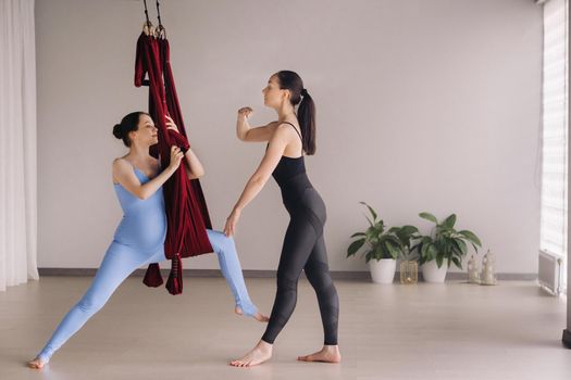 Pregnant girl. A woman with a trainer does yoga in a hammock in the gym. The concept of a healthy lifestyle, motherhood.