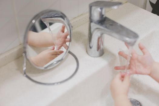 child washing hands under the tap water in the bathroom. kid's hands under stream of water.