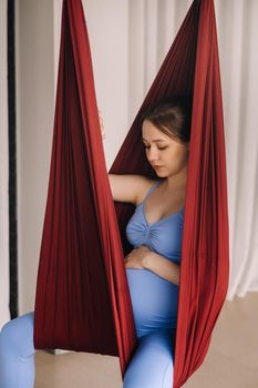 Pregnant girl. A woman does yoga sitting in a hammock in the gym. The concept of a healthy lifestyle, motherhood.