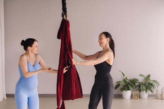 Pregnant girl. A woman with a trainer does yoga in a hammock in the gym. The concept of a healthy lifestyle, motherhood.