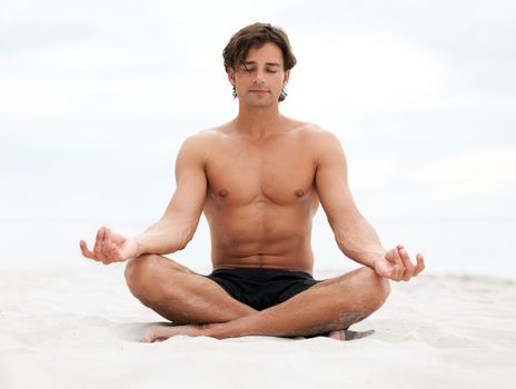 Young handsome man sitting on the beach meditating.
