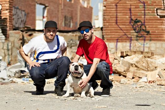 Two urban males kneeling down with a dog in their neighborhood.