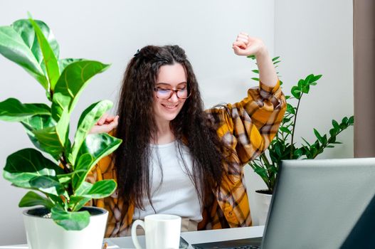Beautiful woman in glasses dancing with joy in the workplace. Woman working at home, undergoing training, watching webinar, online shopping.