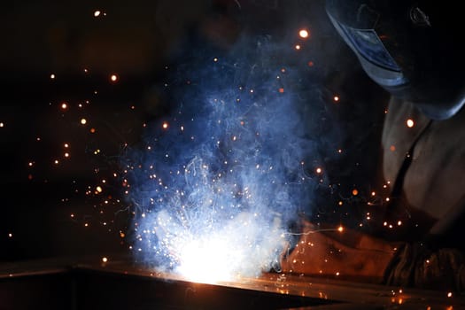 Welder at work. Welding of metal sparks and smoke in the workshop. Industrial Welder With gas Torch in Protective Helmet, welding metal profiles. The welding operation at construction site.