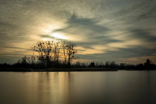 The sun behind the clouds over the frozen lake and trees on the shore, Stankow, Poland